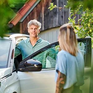 Ein Mann steigt aus dem Auto und unterhält sich mit einer Frau.