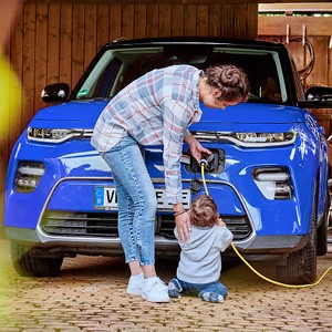 Eine Frau lädt ihr Elektroauto auf. Ihr kleines Kind hilft und hält das Kabel.