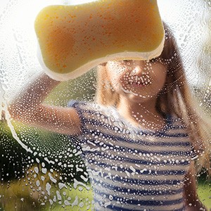 Ein Mädchen putzt mit einem Schwamm ein Fenster.