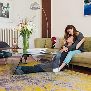 Ein junges Paar sitzt im Wohnzimmer an einem Glastisch.