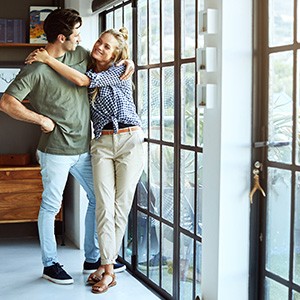 Ein junges Paar blickt aus einer Glastür in den Garten.