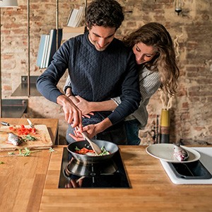 Ein junges Paar kocht Essen auf einem Induktionsfeld.