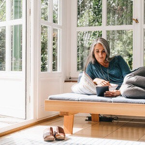 Eine Frau liegt auf einem Sofa in einem hellen Raum und schaut auf ein Tablet.