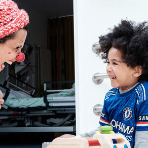 Frau verkleidet als Clown bringt einen kleinen Jungen im Krankenhaus zum Lachen.