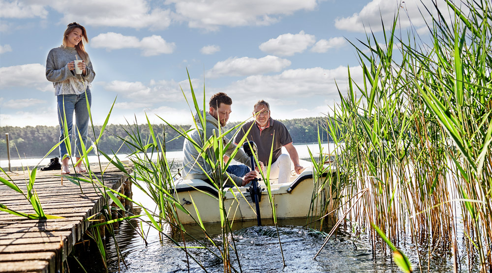 Eine Frau steht auf einem Steg, von dem zwei Männer in ein kleines Boot steigen.