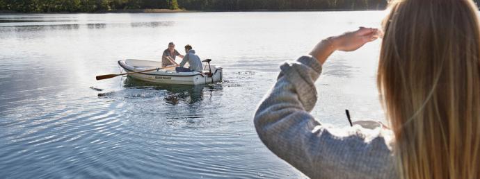 Frau schaut auf einen See. Auf dem See sitzen zwei Personen in einem Ruderboot.