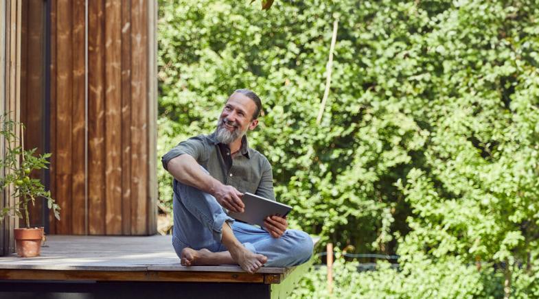 Mann sitzt barfuß auf einer Terrasse aus Holz im Garten.