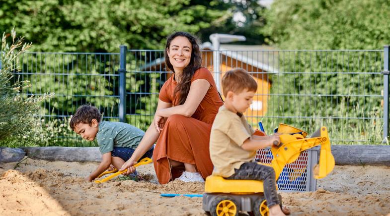 Eine Frau spielt mit zwei Kindern im Sandkasten.