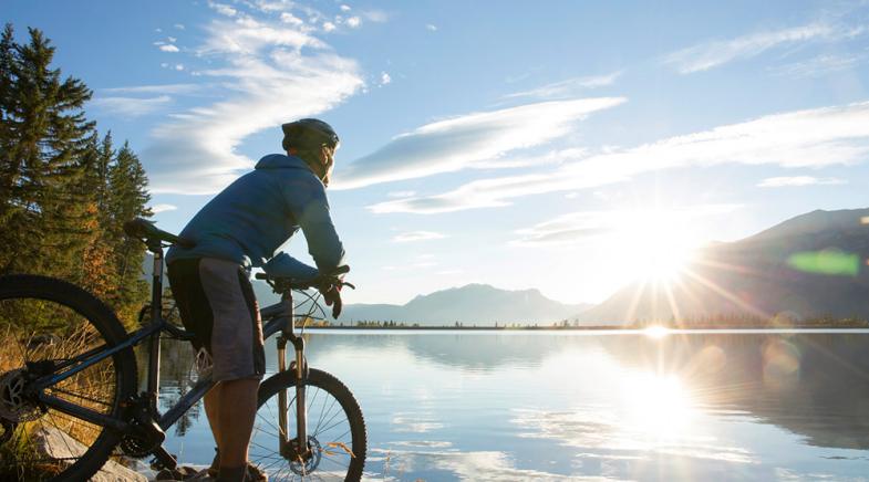 Ein Mann steht mit seinem Fahrrad an einem See.