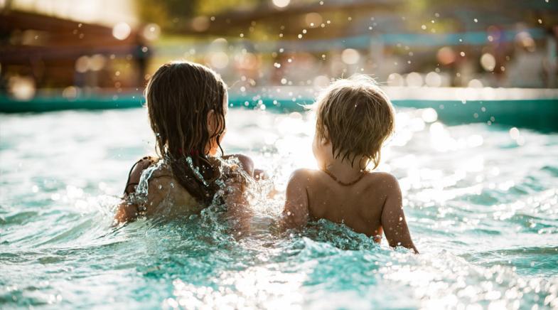 Zwei Kinder sitzen in einem Schwimmbecken.