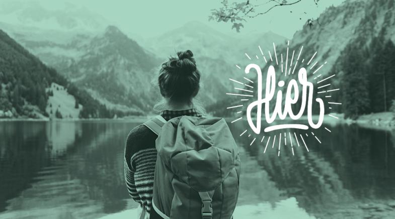 Frau steht mit Rucksack vor einem See in den Bergen. Das Hier Logo weiß im Vordergrund.