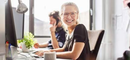 Eine Frau im Büro dreht sich lächelnd zu einer anderen Person.