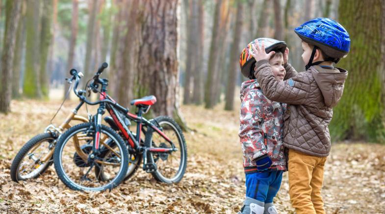 Zwei Kinder stehen im Wald und rücken sich die Fahrradhelme zurecht