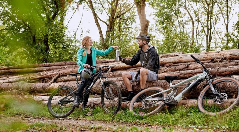 Zwei Fahrradfahrer machen eine Trinkpause im Wald.