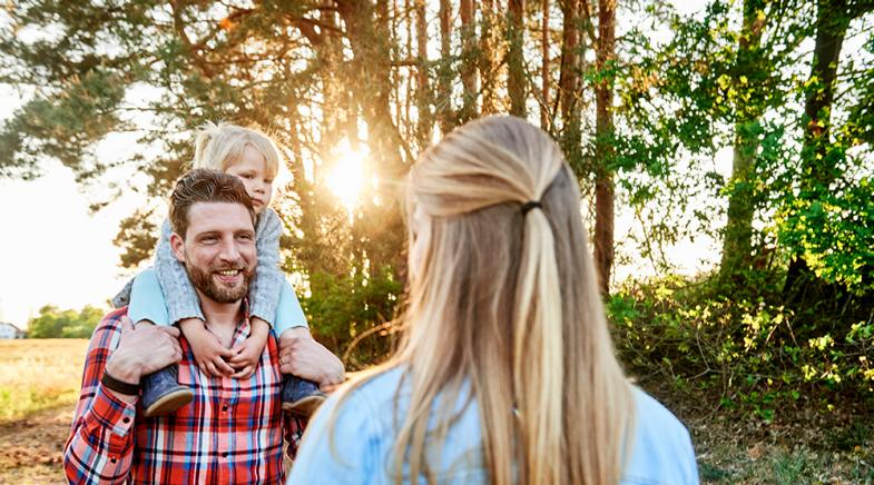 Eine Familie steht vor Bäumen und einem Feld.