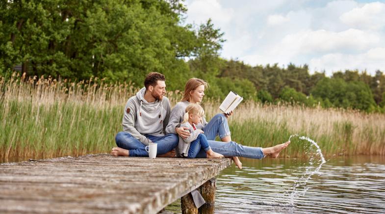 Eine Familie sitzt gemeinsam auf einem Steg und hält die Füße in den See.