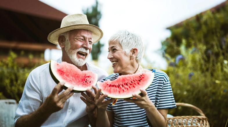 Ein älteres Paar isst Wassermelone und lacht.