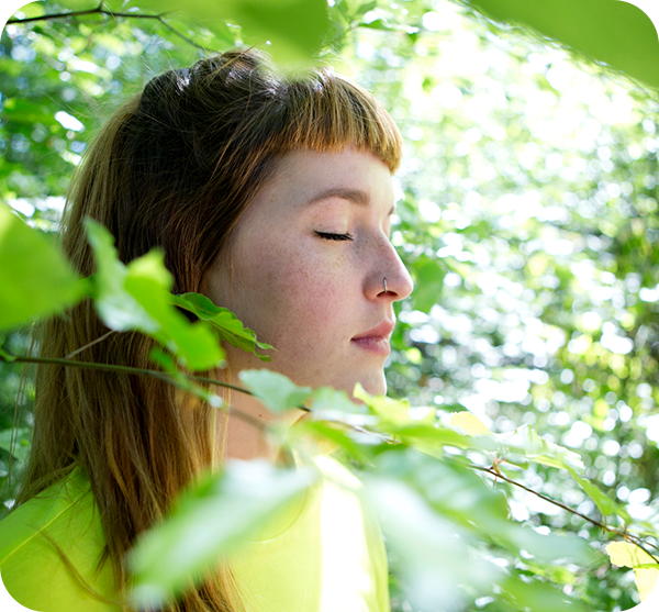 Eine Frau steht mit geschlossenen Augen in der Natur.