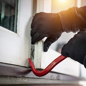 Jemand bricht mithilfe einer Brechstange ein Fenster auf.