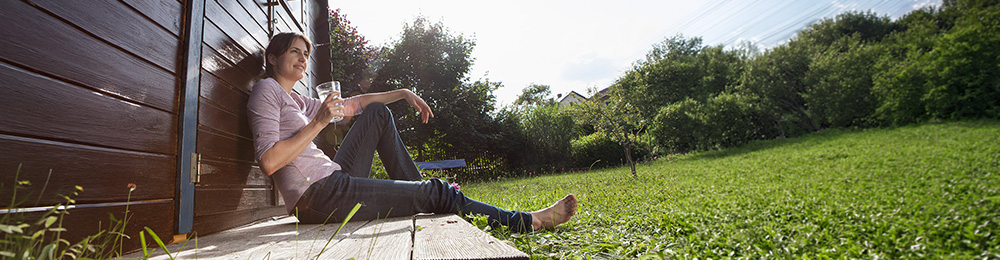 Eine junge Frau sitzt entspannt in der Sonne im Garten.